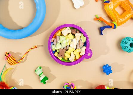 Verschiedene bunte Tierpflegezubehör: Schale, Knochen, Kugeln, Snacks, Maus auf beigem Hintergrund. Gummi- und Textilzubehör für Hunde und Katzen. Stockfoto