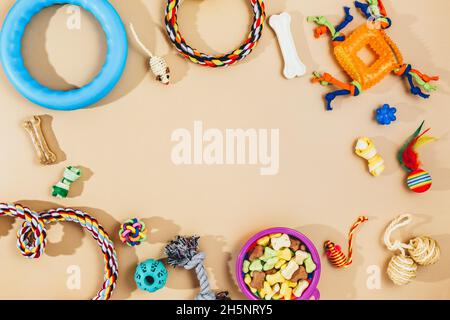 Verschiedene bunte Tierpflegezubehör: Schale, Knochen, Kugeln, Snacks, Maus auf beigem Hintergrund. Gummi- und Textilzubehör für Hunde und Katzen. Stockfoto