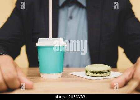 Eine Tasse Espresso, Makronen. Hand des Mannes mit einer Tasse. Kaffeepause im Büro. Holztisch. Geschäftsmann hat Frühstück in einem Café, Getränke Kaffee und Stockfoto