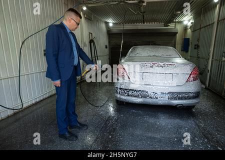 Ein Mann wäscht ein Auto in einer Box kontaktlose Auto waschen Self-Service mit einer Wasserpistole in manuellen Self-Service-Waschstation. Männlich waschen das Auto mit hohen Pre Stockfoto