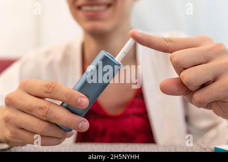 Raucher rauchen Hybrid rauchlose Zigarettengerät, das echte Tabak Nachfüllungen verwendet, Hybrid-Technologie zwischen analogen und elektronischen Zigaretten. Mann füllt Stockfoto