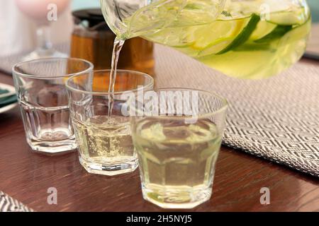 Männliche Hand legte Zitrone in Glasflasche, Mann bereitet, detox gesundes Wasser mit Zitrone und Rosmarin, frische Limonade im Glas auf einem Tisch zu Hause, su Stockfoto