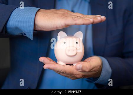Geschäftsmann mit Sparschwein über dunklem Hintergrund. Das Konzept der Einsparung und Anhäufung von Geld. Ein gut gekleideter Geschäftsmann hält ein Sparschwein mit Coi Stockfoto