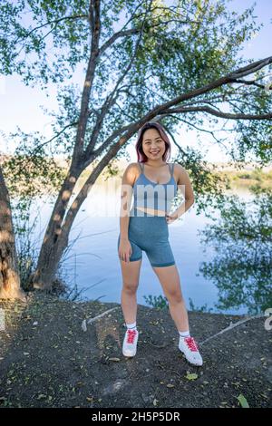 Junge asiatische Frau im strahlenden Sonnenlicht, die am Ufer eines idyllischen Sees sitzt Stockfoto