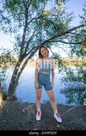 Junge asiatische Frau im strahlenden Sonnenlicht, die am Ufer eines idyllischen Sees sitzt Stockfoto