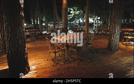 Nachtaufnahme von Holzterrasse einer eleganten Bar im Freien, beleuchtet von kleinen Lampen in den Bäumen, die über die Terrasse steigen Stockfoto