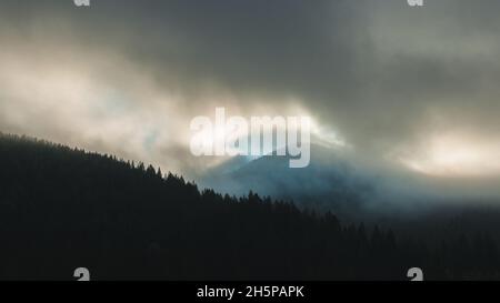 Die Strahlen der aufgehenden Sonne brechen durch den Morgennebel in den Bergen. Silhouette Landscape Foto Stockfoto