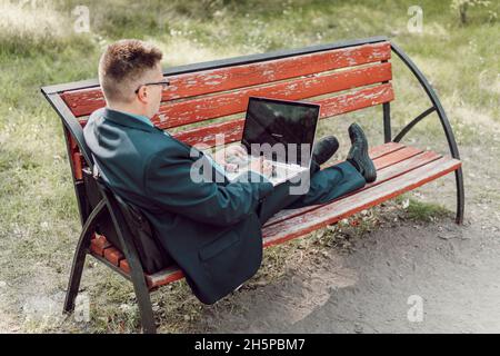 Mann mit Laptop im Sommer Park an hellen Tag. Geschäftsmann sitzt auf der Bank und beobachten auf dem Laptop im Stadtpark im Freien. Internetverbindung A Stockfoto