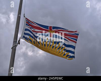 Provinzflagge von British Columbia mit Krone in der Mitte der Royal Union Flagge und untergehende Sonne unten auf Fahnenmast in Port Hardy, Kanada. Stockfoto