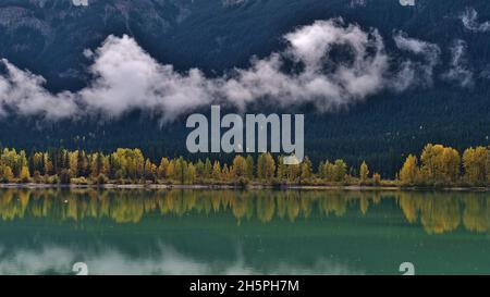 Wunderschöne Aussicht auf den Moose Lake im Mount Robson Provincial Park, British Columbia, Kanada mit niedrigen Wolken und gelb gefärbten Bäumen, die sich im Wasser spiegeln. Stockfoto