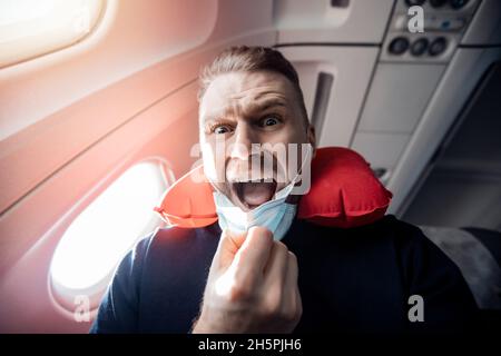 Konzept Aerophobie oder Aviophobie. Angst vor Angst fliegen im Flugzeug und Höhe Tourist Mann in sichere medizinische Maske. Stockfoto