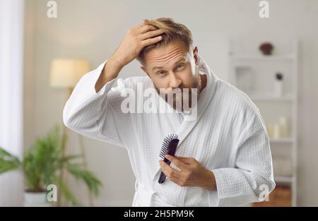 Ein hübscher Mann, der mit dem Problem des Haarausfalls konfrontiert war und in seinem Badezimmer in einen Spiegel schaute Stockfoto