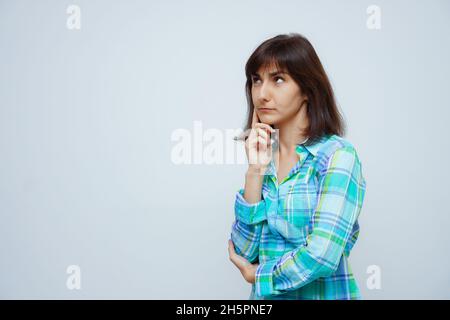 Nachdenklich nette kaukasische Frau runzelt das Gesicht, schaut auf, isoliert auf grauem Hintergrund Stockfoto