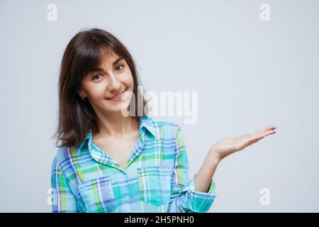 Attraktive kaukasische Frau öffnen die Hände mit der Handfläche nach oben und hält etwas auf isoliertem grauem Hintergrund Stockfoto