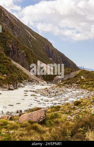 Wandern Sie in einem grünen Tal in den südlichen Alpen vom Hooker Lake zum Mller Lake. Entlang eines kleinen Flusses zwischen den Hügeln. Südinsel, Neuseeland. Stockfoto