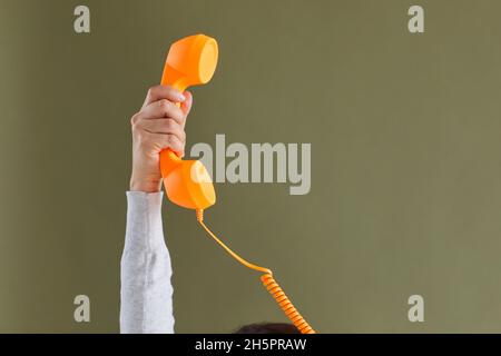 Menschliche Hand mit orangefarbenem Festnetzempfänger vor grünem Hintergrund des Kopierbereichs Stockfoto