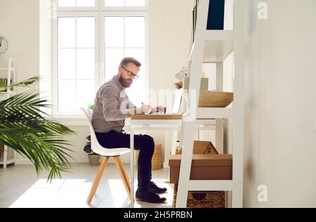 Seriös fokussierter Geschäftsmann, der an einem wichtigen Arbeitsprojekt in seinem hellen Home Office arbeitet. Stockfoto