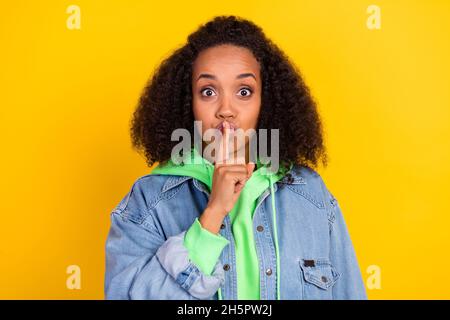 Foto von schönen attraktiven afro Frau tragen Denim Jacke Finger Mund fragen Stille isoliert gelbe Farbe Hintergrund Stockfoto