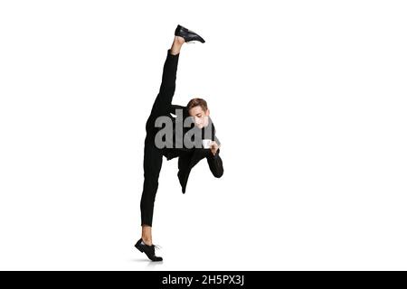 Junger Mann in schwarzem Geschäftsanzug, der in einer Garnstrang steht und auf weißem Hintergrund isoliert Kaffee trinkt. Kunst, Bewegung, Aktion, Flexibilität Stockfoto
