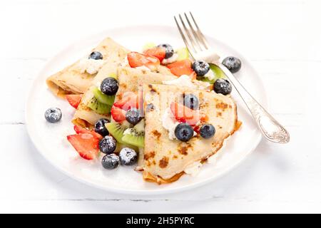 Süße Crepes mit Beeren und Creme auf weißem Holzhintergrund. Hausgemachtes Food-Konzept. Stockfoto
