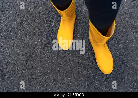 Füße in Gummistiefeln auf dem nassen Asphalt. Stockfoto