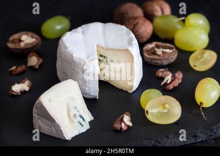 Brie-Käsesorte. Weicher Käse mit Trauben und Walnüssen auf schwarzem Hintergrund Stockfoto