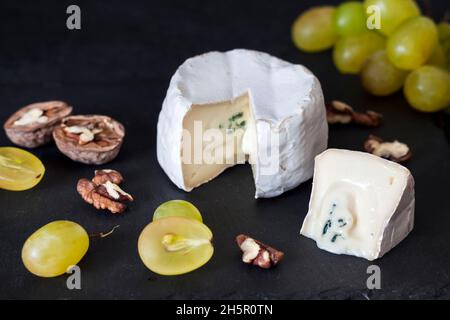 Brie-Käsesorte. Weicher Käse mit Trauben und Walnüssen auf schwarzem Hintergrund Stockfoto