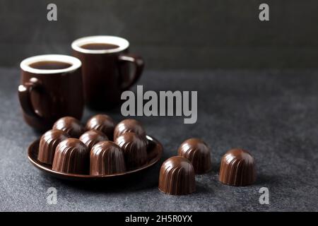 Schokolade Bonbons auf einem Teller und zwei Tassen heißen Kaffee auf schwarzem Hintergrund mit Platz zum Kopieren Stockfoto