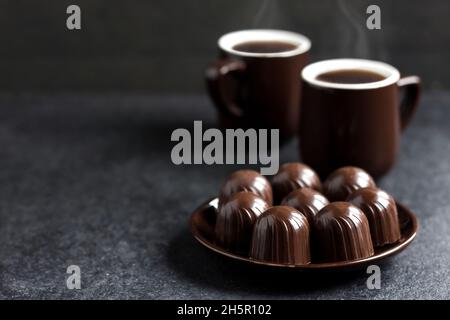 Schokolade Bonbons auf einem Teller und zwei Tassen heißen Kaffee auf schwarzem Hintergrund mit Platz zum Kopieren Stockfoto