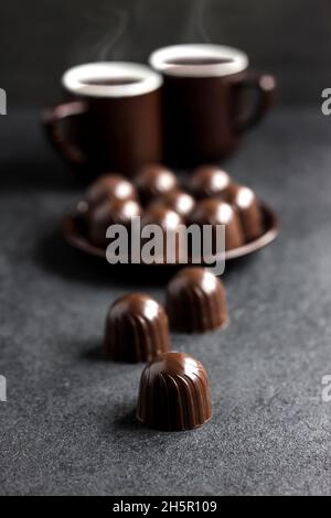 Schokolade Bonbons auf einem Teller und zwei Tassen heißen Kaffee auf schwarzem Hintergrund mit Platz zum Kopieren Stockfoto