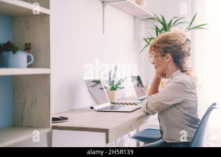 Frau, die zu Hause mit einem Laptop auf einem Desktop-Arbeitsplatz arbeitet. Glückliche moderne Frauen benutzen Computer im Wohnzimmer. Smart arbeiten junge Dame Konzept lif Stockfoto