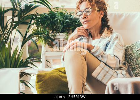 Attraktive Frau Porträt sitzt auf einem Stuhl im Garten zu Hause suchen und denken. Freilufthaus Freizeitbeschäftigung weibliche Menschen. Erwachsene Dame mit Stockfoto