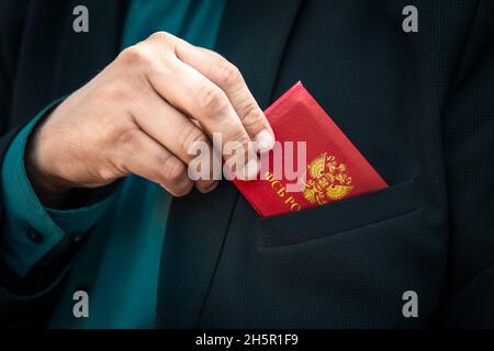 Der rote Personalausweis des FSB. Mann Mit Id-Karte. Ein Mann in einem blauen Anzug zeigt einen roten Ausweis oder einen Pass. Die Hand eines Mannes in einem blauen Anzug nimmt eine rote ID heraus. Ca Stockfoto