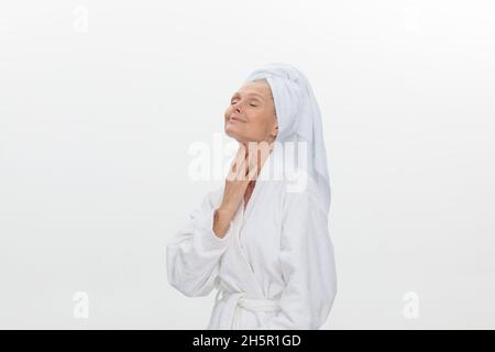 Eine schöne reife Frau, die einen weißen Bademantel und ein Handtuch um ihren Kopf gewickelt trägt. Stockfoto