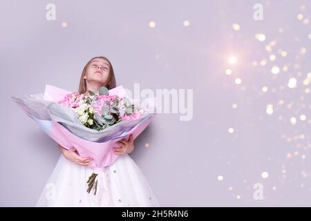 Ein Mädchen in einem weißen Kleid steht zur Seite und hält einen Blumenstrauß, der ihr Gesicht bedeckt. Urlaubskonzept, Hintergrund in Lichtern. Hochwertige Fotos Stockfoto