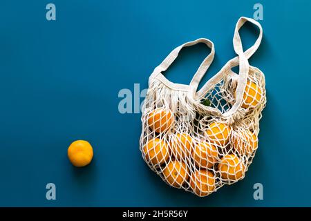 Mandarinen oder Mandarinen Früchte in Baumwolle umweltfreundliche Netztasche auf blauem Hintergrund. Konzept von Zero Waste, plastikfreiem Einkaufen oder Öko-Food. Draufsicht. Stockfoto