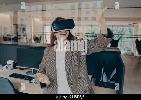 Weibliche Büroangestellte verwenden ein Virtual-Reality-Headset, um Dateien bei der Arbeit zu visualisieren und zu durchsuchen Stockfoto