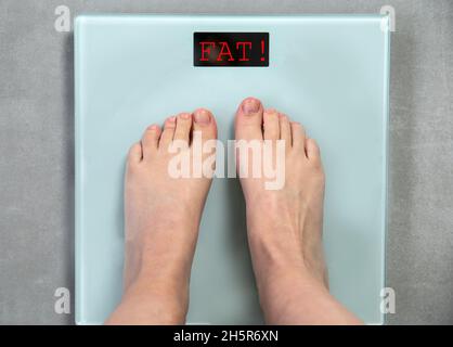 Füße auf digitaler Waage mit Wort FETT Draufsicht, Nachricht ungesunder Lebensstil, Gewicht zu verlieren Nachricht, Hilfe Konzept Stockfoto