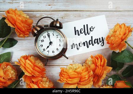 Hello Monday Karte und Wecker mit oranger Blumendekoration auf Holzhintergrund Stockfoto