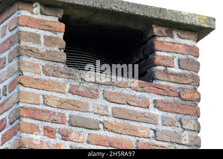 Ein Porträt des Öffnungs- oder Rauchausgangs im oberen Teil eines hohen gemauerten, roten Ziegelschornsteins auf einem Dach eines Hauses an einem bewölkten Tag. Stockfoto