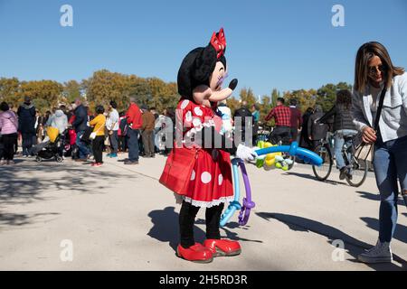 Madrid, Spanien - 09. Nov 2021: Ein Straßenkünstler, der als Minie Mouse gekleidet ist, gibt Luftballons zum Betteln im Retiro Park Stockfoto