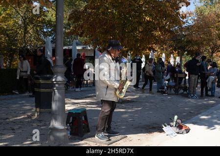 Madrid, Spanien - 09. Nov 2021: Ein älterer Mann, ein Straßenmusiker, spielt Saxophon und bittet um Almosen im Retiro Park Stockfoto