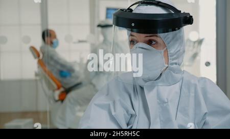 Nahaufnahme der zahnärztlichen Krankenschwester mit Hazmat Anzug arbeiten an der Mundpflege in der Stomatologie Klinik. Professionelle Assistentin mit zahnmedizinischen Geräten hilft Zahnarzt mit Patientenberatung Stockfoto