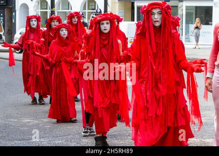 Straßenfoto einer Gruppe von Darstellern des „Invisible Circus“ der Roten Brigade bei einer Demonstration zum Klimawandel, die in einer Reihe durch die Straßen läuft. Stockfoto