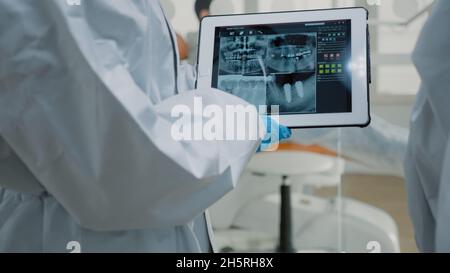 Nahaufnahme der zahnärztlichen Röntgenaufnahme auf dem digitalen Tablet-Bildschirm in der Hand von Kieferorthopäden mit psa-Anzügen. Gerät mit moderner Technologie für professionellen Mundschutz und Beratung eingesetzt Stockfoto
