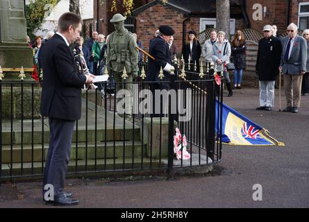 Syston, Leicestershire, Großbritannien. November 2021. Der Standard wird während der gedenkfeiern zum Waffenstillstandstag im Syston war Memorial in der Nähe eines lebensgroßen gestrickten Soldaten gesenkt. Credit Darren Staples/Alamy Live News. Stockfoto