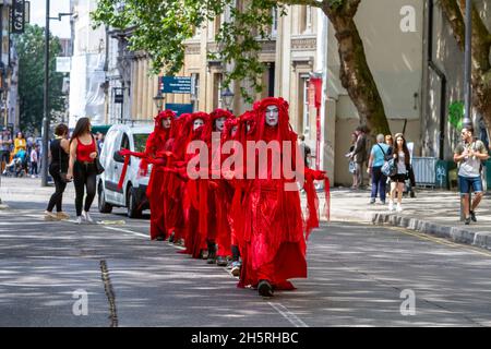 Straßenfoto einer Gruppe von Darstellern des „Invisible Circus“ der Roten Brigade, die eine Demonstration zum Klimawandel durch die Straßen einer Stadt führen. Stockfoto