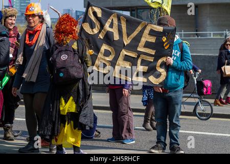 Straßenfoto von Demonstranten bei einer Klima-Notstandsskundgebung mit einem großen Transparent „Rette die Bienen“ und in Kostüm. Banner ist Mittelbild Stockfoto