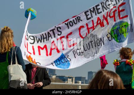 Straßenfoto einer Gruppe von Demonstranten des Klimawandels mit großem selbstgemachten Banner mit Rücken zur Kamera. Einige Gebäude sind dahinter zu sehen. Stockfoto