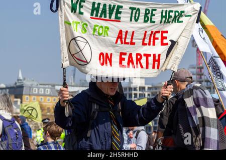 Straßenfoto eines Mannes, der ein Banner bei einer Demonstration zum Klimawandel in der Mitte hält, mit anderen Protestierenden, Plakaten und Flaggen. Stockfoto